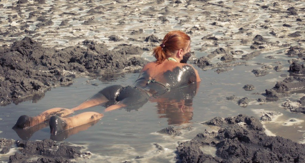 Голая нудистка на прибережных скалах принимает волны воды на тело